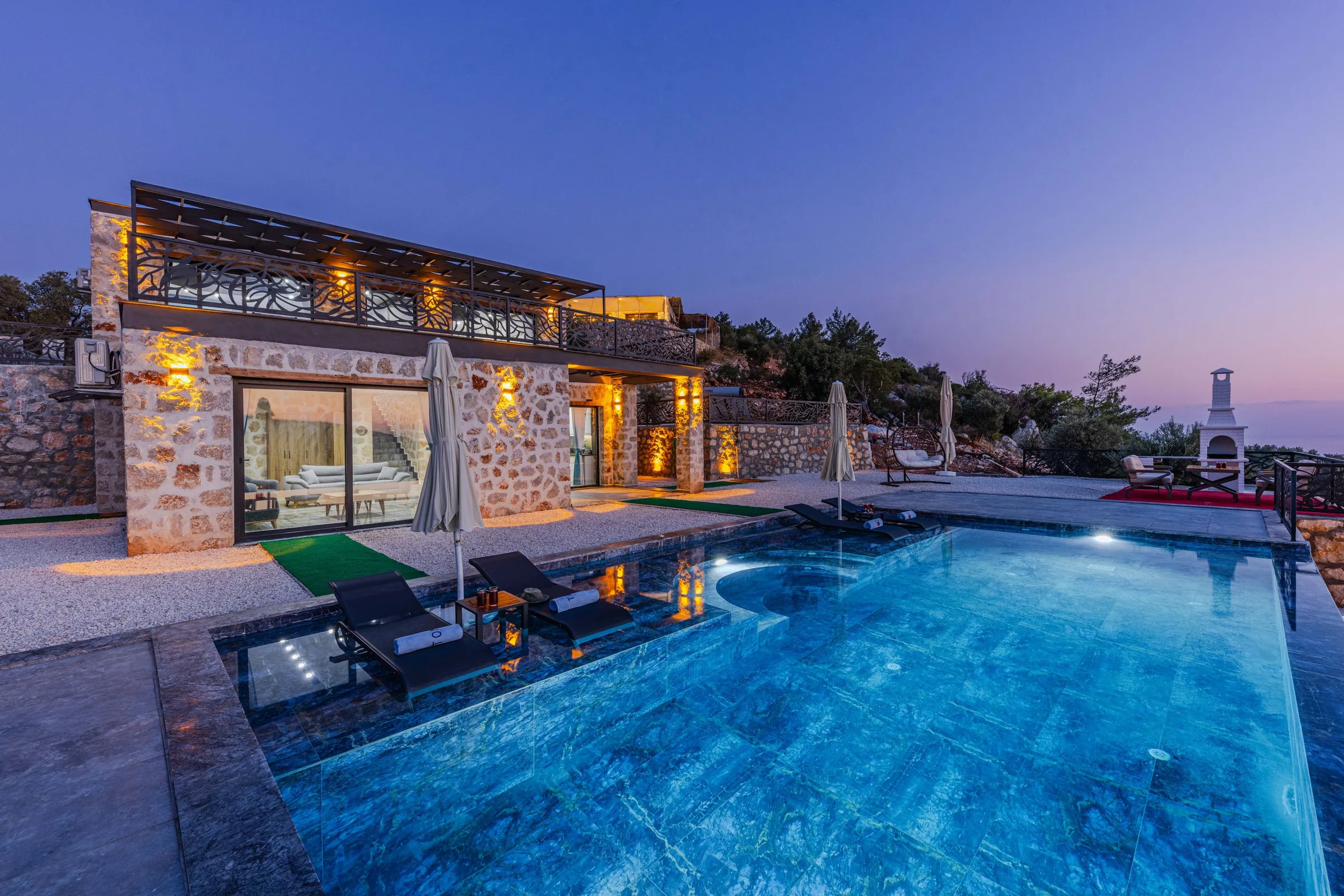 Stone villa and illuminated pool at dusk